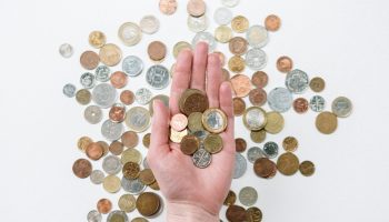 An open hand holds various coins on a white surface, symbolizing finance and currency exchange.