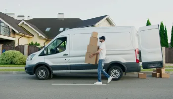 Man unloading cardboard boxes from a delivery van in a suburban neighborhood street.